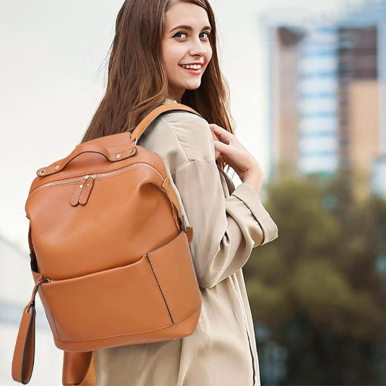 Sac a dos à langer couleur marron porté en bandoulière sur l'épaule d'une demoiselle.