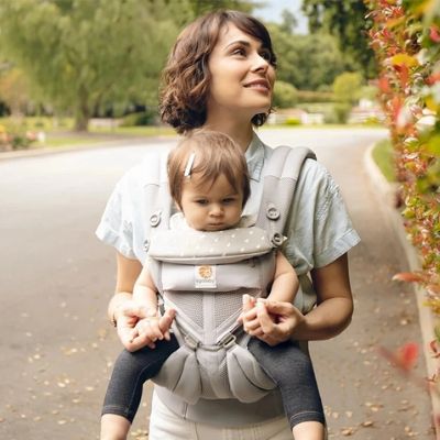 Maman qui porte son bébé fille dans un porte bébé gris à l'extérieur se promenant durant l'automne.