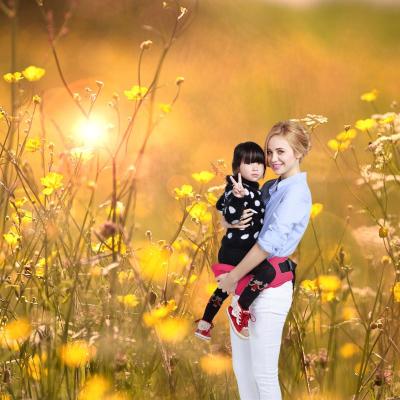 Porte bébé rose avec petite fille dessus et sa mère qui la porte ans un champs.