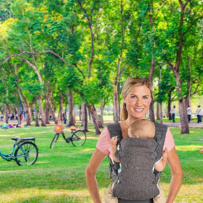 Maman qui porte son bébé dans son porte bébé dans un parc et ils sont joyeux.