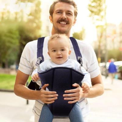 Père qui porte son enfant dans un porte bébé bleu vu de face à l'extérieur.