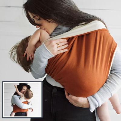 Porte bébé genre kangourou orange et beige avec son enfant installé dedans.