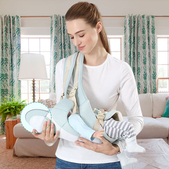 Maman portant son bébé fille en position couché dans un porte bébé vert dans son salon.