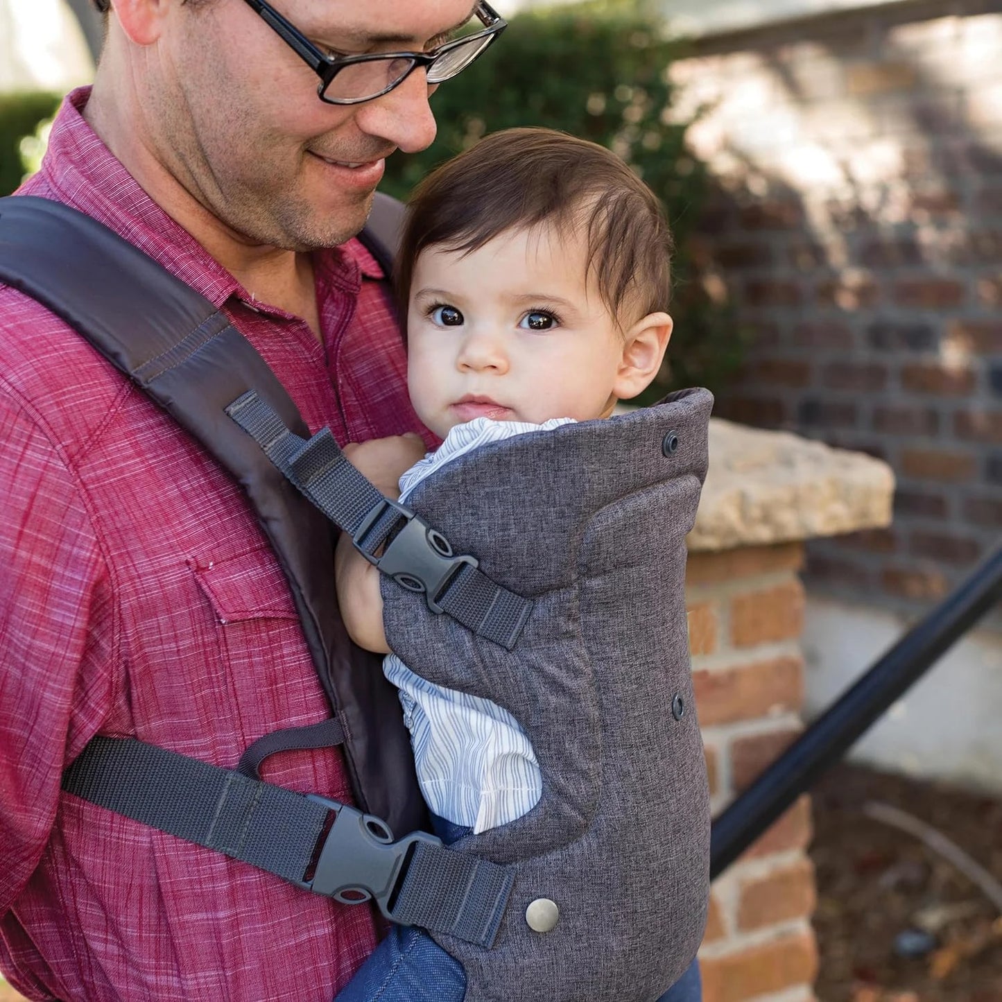 Papa souriant portant son bébé dans son porte bébé en position ventral.