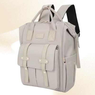 Présentation d'un sac à dos à langer beige sur un fond beige contenant plusieurs pochettes, avec prise en main ou bandoulières pour le transformer en sac à dos.