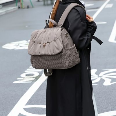 Sac à dos à langer gris montrant qu'on peut le porter en bandoulière.