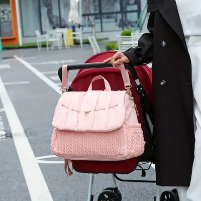 Sac à dos à langer rose accroché sur la poignée d'une poussette.