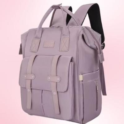 Présentation d'un sac à dos à langer mauve sur un fond mauve avec plusieurs pochettes, avec prise en main ou bandoulières pour le transformer en sac à dos.