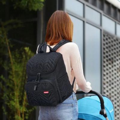 Sac à langer bébé présenté en sac à dos avec maman poussant une poussette.