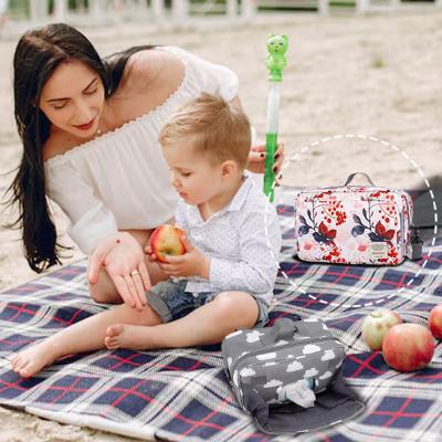 Sac à langer avec des motifs de fleurs démontrant une maman et son bébé en pique-nique à l'extérieur.