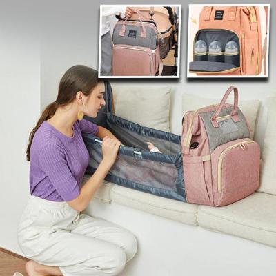 Sac à langer rose, bébé couché à l'intérieur et maman à ses côtés qui en prend soin et en démonstration, des bouteilles de lait que l'on peut mettre dans le sac.